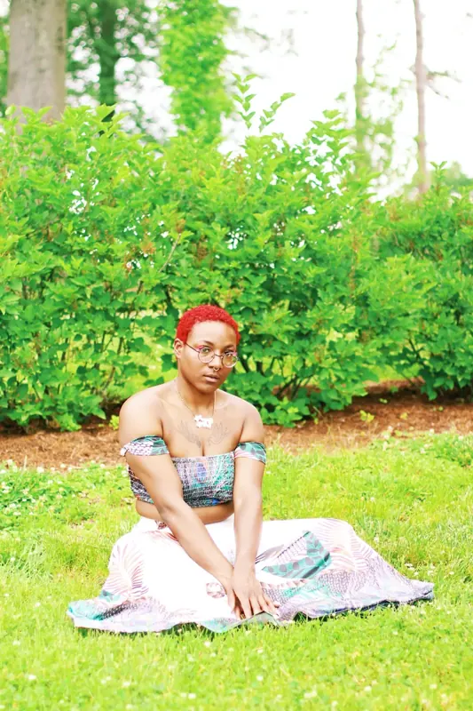 Peach Fuzz with red hair sitting on the grass in a leafy garden in a pastel skirt